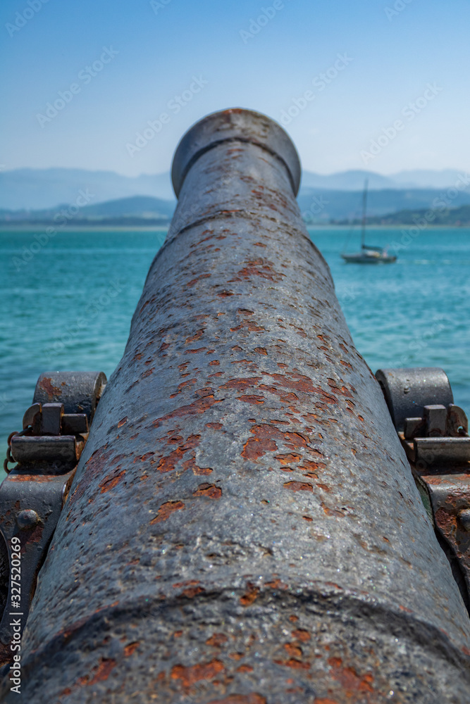Antique old cannon pointing to the sea with blurred boat Antique old cannon pointing to the sea with blurred boat