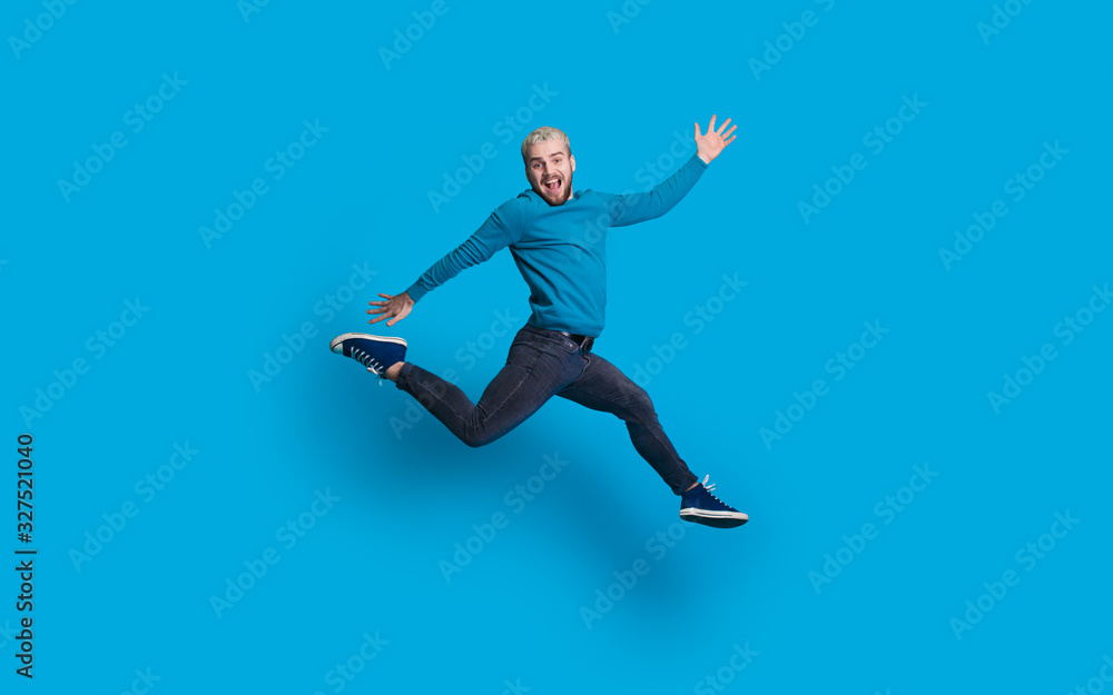 Caucasian man with blonde hair and beard dressed in blue is jumping and imitate running on a blue wall Caucasian man with blonde hair and beard dressed in blue is jumping and imitate running on a blue wall