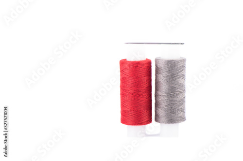 Close-up photo of a spool with red and gray thread and a needle isolated over white background.