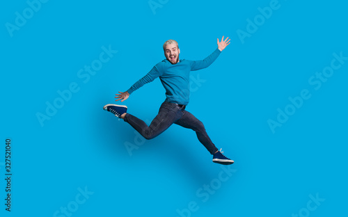 Wallpaper Mural Caucasian man with blonde hair and beard dressed in blue is jumping and imitate running on a blue wall Torontodigital.ca