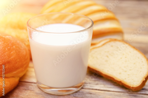 Glass of milk close up, rolls, sliced loaf on a wooden background