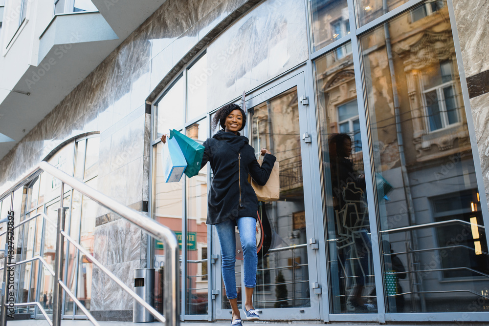 Beautiful curly haired afro-american woman standing in a shopping mall with coloured shopping bags in hands.