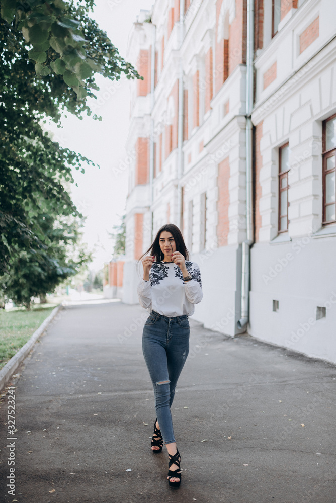 a young girl with brown hair in a white blouse and blue jeans walks down the street