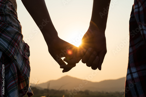 Close up of loving couple holding hands while walking at sunrise sunset in the meadow mountain in background. Valentine's Day and love concept.