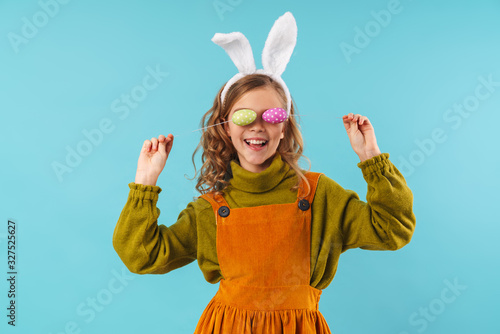 Photo of joyful blonde girl making fun with colorful eggs