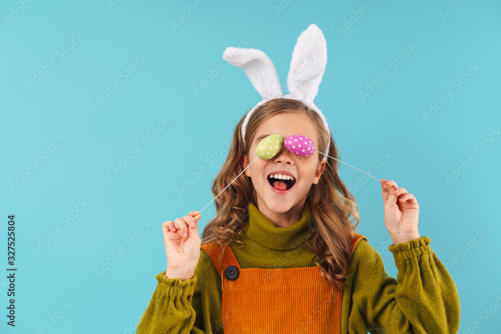 Photo of joyful blonde girl making fun with colorful eggs
