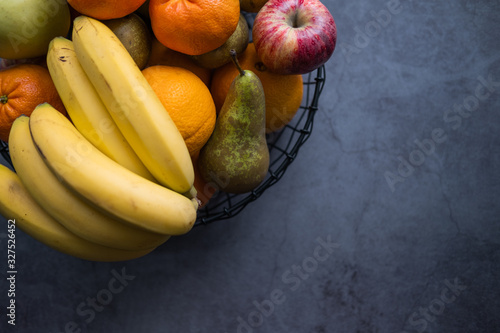 Apples, bananas, pears, tangerines and oranges on a fruit bowl on concrete background. Healthy food. Top view. Copy space.