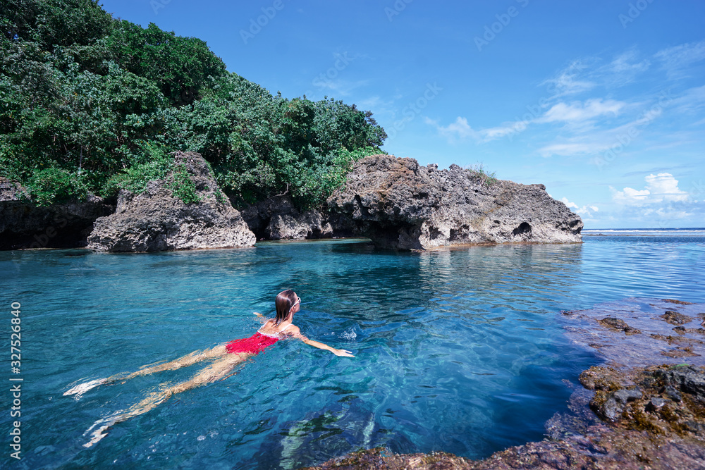 Summer vacation. Beautiful young woman in red swimsuit swimming at sea natural pool.