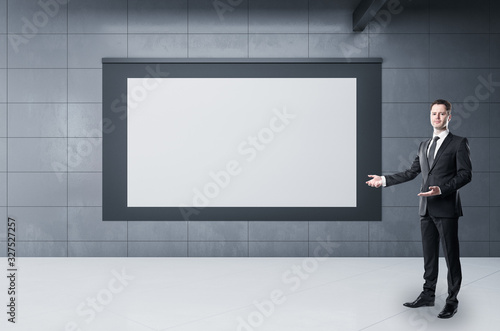 Businessman standing in subway station with blank poster on gray wall