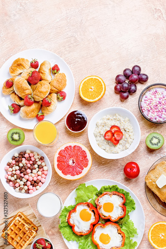 Continental breakfast with cereal, fried eggs, croissants, fruits and drinks on textured table, copy space. Table top with various healthy snacks and foods on rustic background