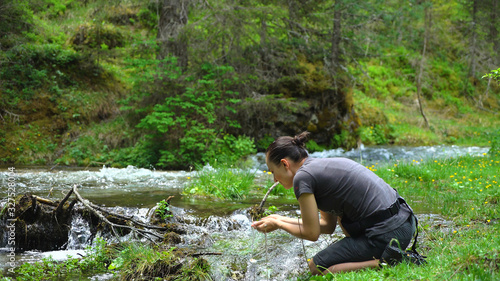 Young hiker woman drinking stream water in the forrest