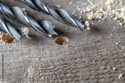 Drills from an electric drill lie on a board near the drilled hole. Joinery and construction work close up. Wood chippings fly off a metal drill. Handyman bores holes into a wooden board.   photo