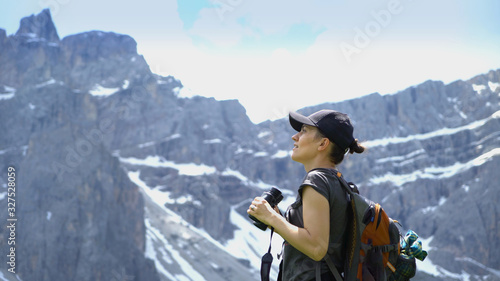 Hiker woman looking with binoculars enjoying spectacular view on mountain top, Dolomites, Italy