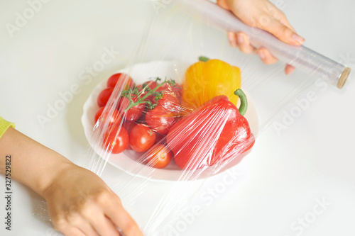 Fotografija Woman using food film for food storage on a white table