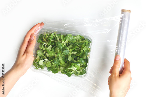 Woman using food film for food storage on a white table. Roll of transparent polyethylene food film for packing products.