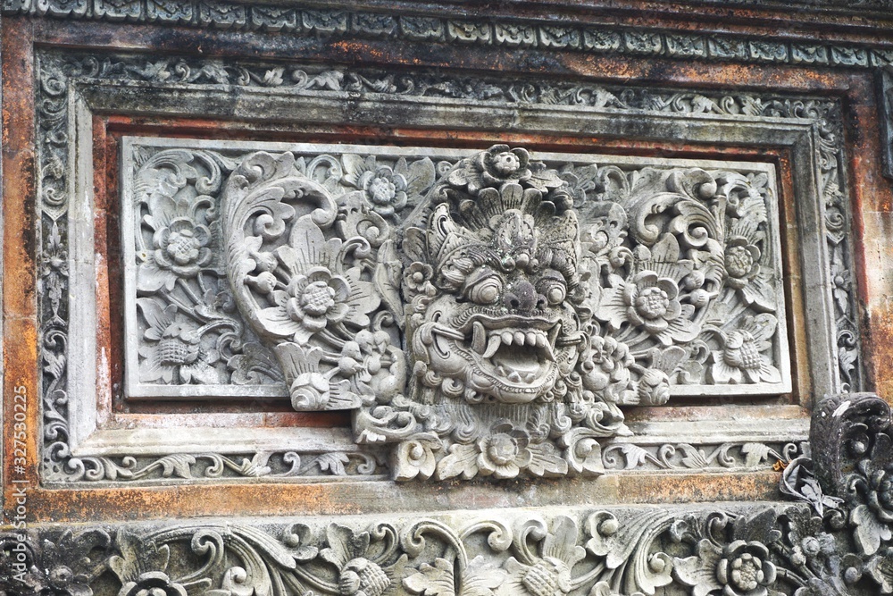 Carved stone smiling demon face on an ancient temple wall in Bali Indonesia