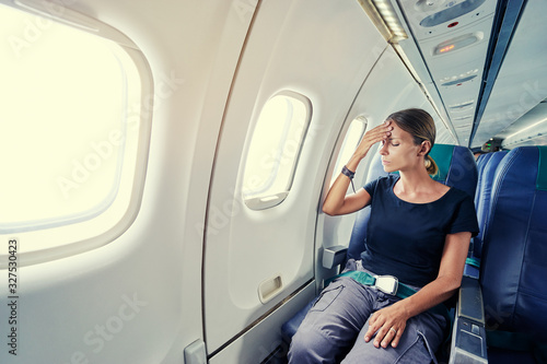 Fear of flying woman in plane airsick with stress headache and motion sickness or airsickness. Person in airplane with aerophobia scared of flying being afraid while sitting in airplane seat. photo