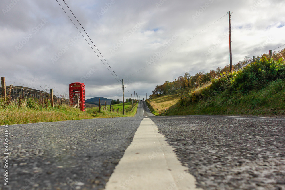 road through a rural area of Scotland, you can see in the distance a red telephone box