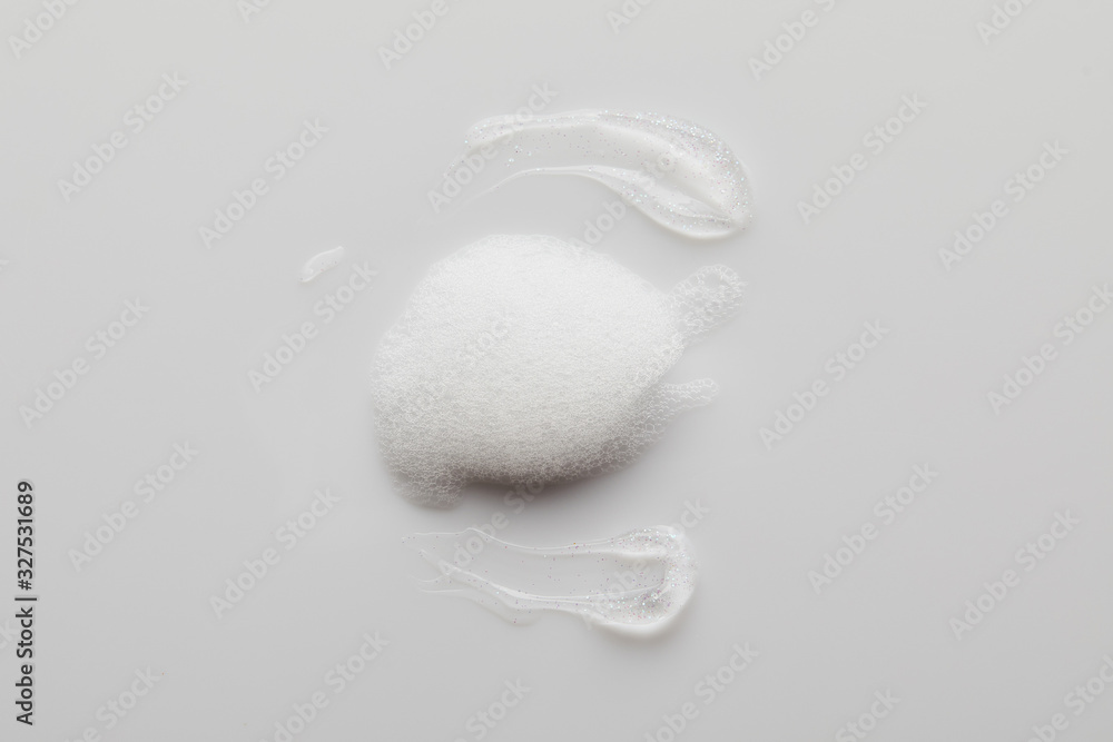 Fototapeta premium Top view of gel brushstrokes with soap foam on grey background