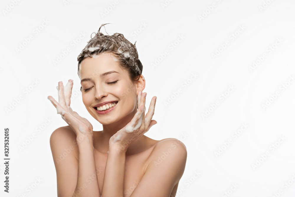 smiling girl with soapy hair and closed eyes holding hands near face isolated on white - obrazy, fototapety, plakaty 