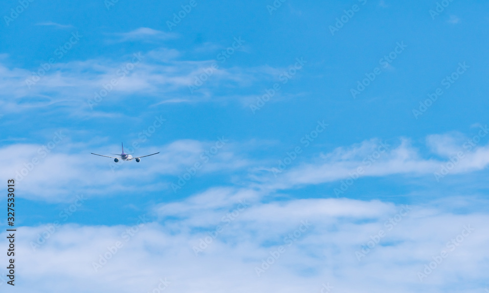 Commercial airline flying on blue sky and white fluffy clouds. Airplane flying on sunny day. Rear view of international flight passenger plane. Summer vacation travel abroad. Air transportation.