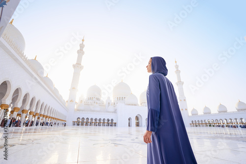 Traveling by Unated Arabic Emirates. Woman in traditional abaya standing in the Sheikh Zayed Grand Mosque, famous Abu Dhabi sightseeing. photo