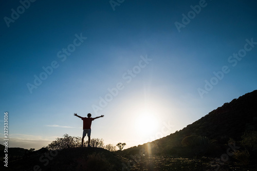one man at the sunset after running session in the hillside with opened arms looking at the sun - fitness and healthy lifestyle and concept