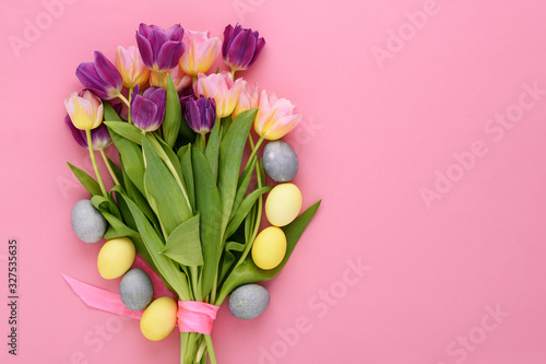 bouquet of pink and lilac tulips and Easter pastel yellow, blue eggs on pink background with copy space, Easter bouquet concept
