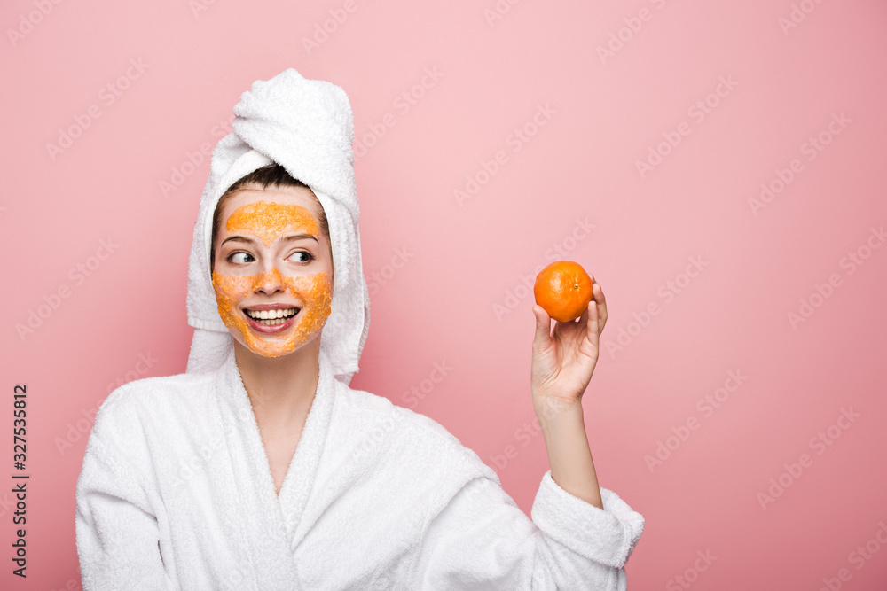 happy girl with citrus facial mask looking at tangerine isolated on pink happy girl with citrus facial mask looking at tangerine isolated on pink