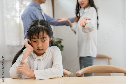 Sad Asian girl sitting alone in dining table while parents quarreling behind his back at home.problem in family and bad relations