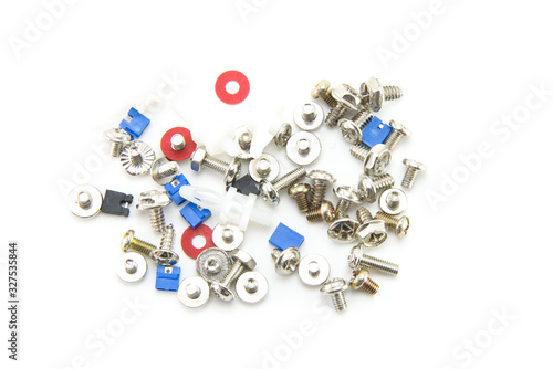 Small bolts, screws and nuts are scattered interspersed with red washers and jumpers in blue and black for the computer. Fasteners for electronics assembly. White isolated background. Close-up.