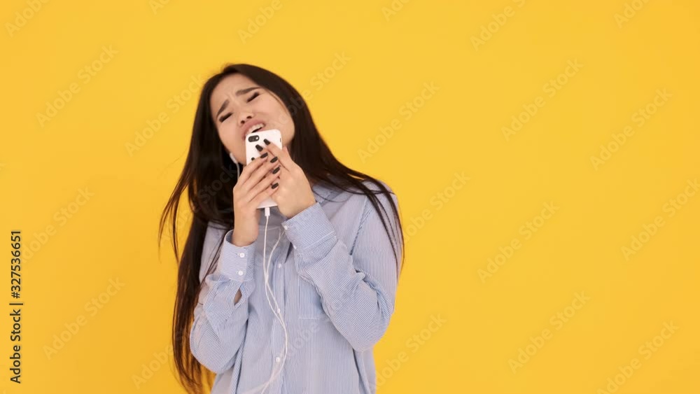 Asian girl in headphones on yellow background sings karaoke on phone and dancing Asian girl in headphones on yellow background sings karaoke on phone and dancing