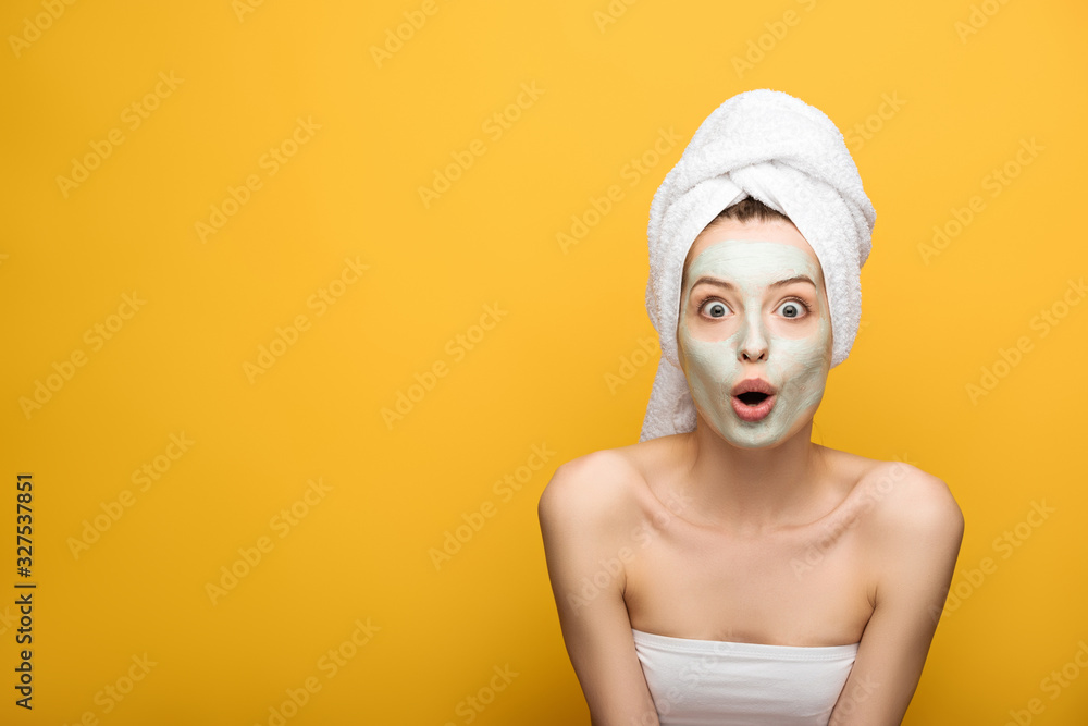 shocked girl with nourishing facial mask and towel on head looking at camera on yellow background shocked girl with nourishing facial mask and towel on head looking at camera on yellow background