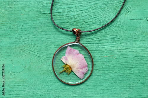 handmade epoxy resin jewelry. pendant, rose in copper frame. dried flowers. herbarium, oshibana, phytotherapy. on green wooden background