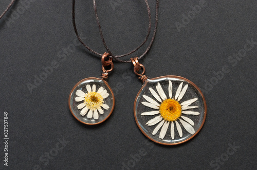 handmade epoxy resin jewelry. pendant, camomile in copper frame. dried flowers. herbarium, oshibana, phytotherapy. isolated on black background