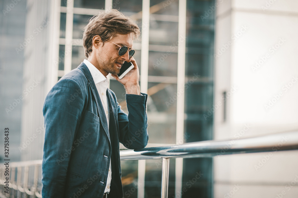 Handsome man walking on a bridge and talking on the phone. Happy smiling young businessman standing outside and having conversation on the phone with urban background. Handsome man walking on a bridge and talking on the phone. Happy smiling young businessman standing outside and having conversation on the phone with urban background.