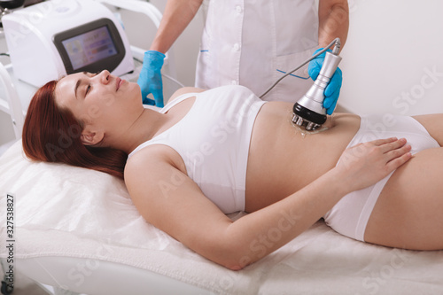 Young woman getting rf-lifting treatment by cosmetologist at beauty salon. Weightloss, fat burning concept photo