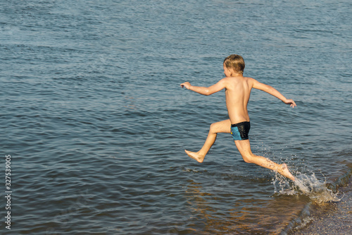 The boy runs and jumps into the sea water.