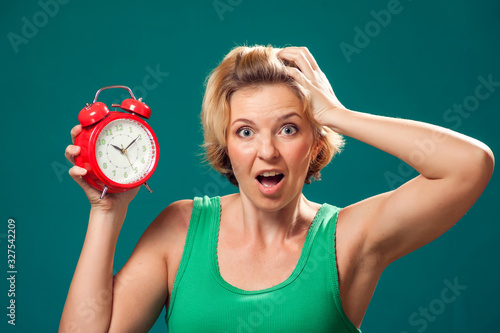 A portrait of surprised woman holding alarm clock. People and emotions concept