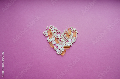 Fototapeta Naklejka Na Ścianę i Meble -  White and yellow pills on a pink background. Dosage of medication. Assorted pills in the shape of a heart. oral contraceptives. Cardiology