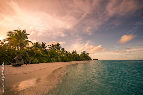 Tranquil tropical beach landscape. Relaxing sunset colors. Beautiful sunset over the sea with a view at palms on the white island beach