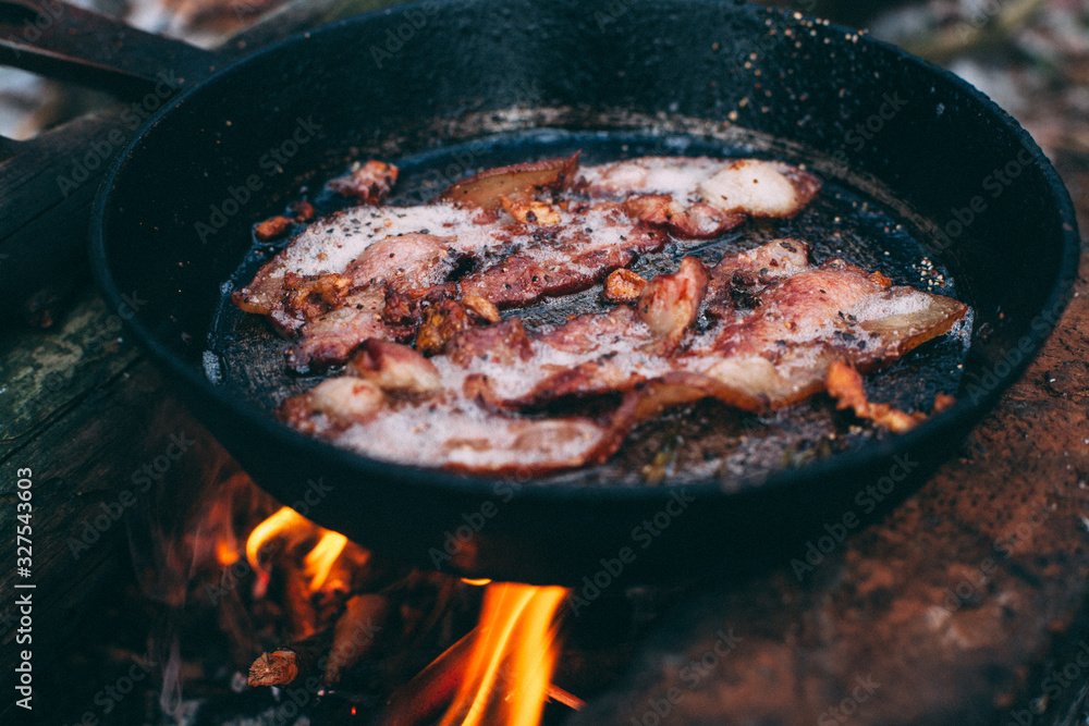 Slices of fried bacon in a pan. Food in a forest camp. Cooking on fire. Picnic in the nature. Grilled food on nature.. Slices of fried bacon in a pan. Food in a forest camp. Cooking on fire. Picnic in the nature. Grilled food on nature..
