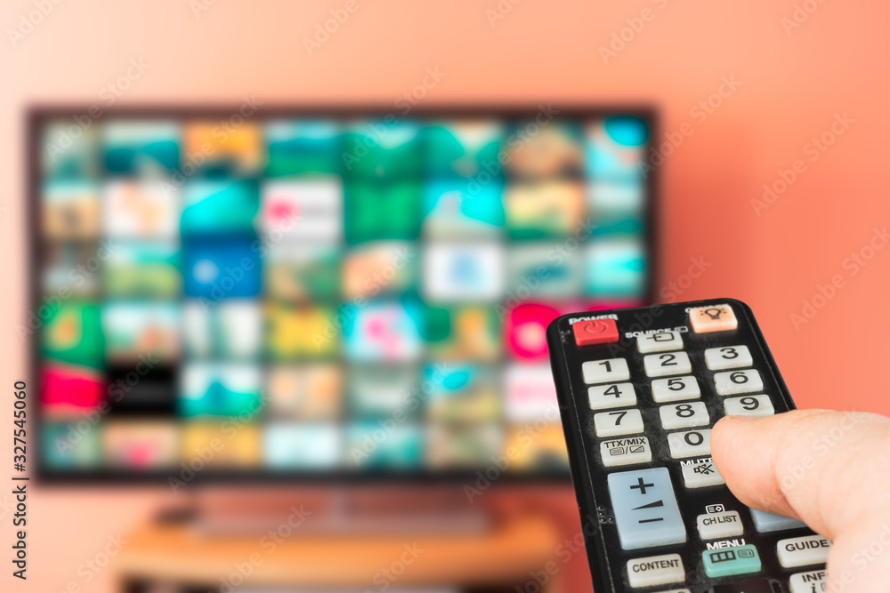 Caucasian man choosing what to watch on TV at home. Video on demand or VOD abstract concept. Changing channels and adjusting volume with television remote control.