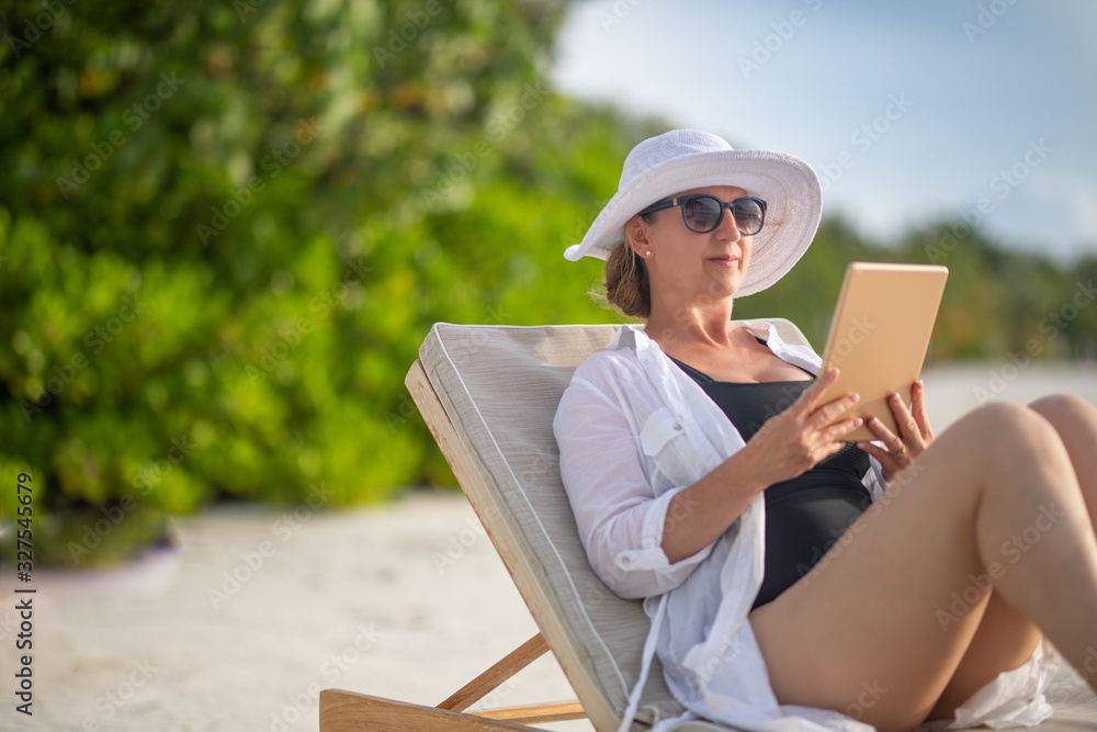 Woman with tablet computer on the beach sitting in the deck chair. Home office concept, passive income concept