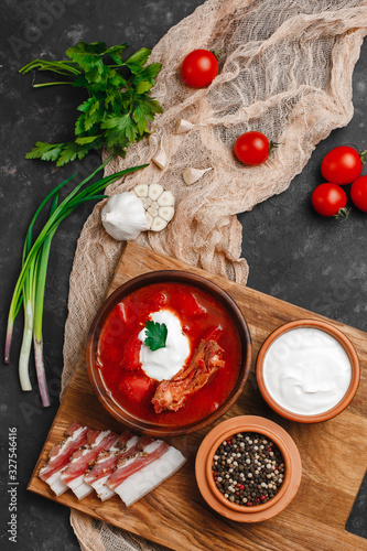 Ukrainian borsch. Beetroot soup. Ukrainian cuisine.In a wooden plate with salted bacon, bread and herbs. On dark background. The view from the top. Free space for your text. A bowl of red beet soup wi