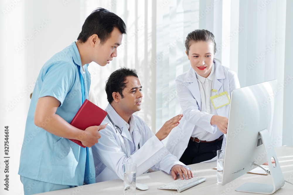 Multi-ethnic medical team gathered at computer screen to discuss virus outbreak statistics Multi-ethnic medical team gathered at computer screen to discuss virus outbreak statistics