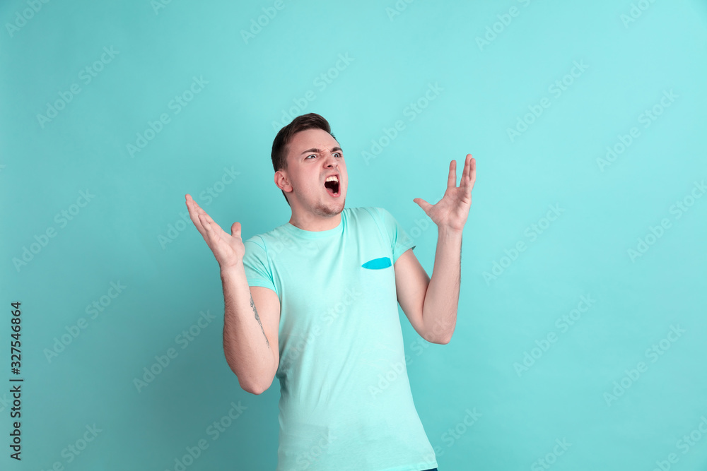 Angry screaming. Caucasian young man's portrait isolated on blue studio background. Beautiful male model in casual style, pastel colors. Concept of human emotions, facial expression, sales, ad. Angry screaming. Caucasian young man's portrait isolated on blue studio background. Beautiful male model in casual style, pastel colors. Concept of human emotions, facial expression, sales, ad.