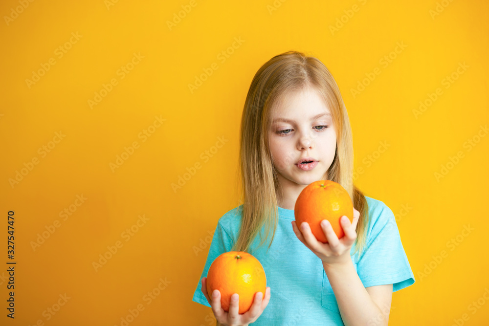 Cute baby 8 years old on an orange background, blonde pretty girl with appelsins in her hands smiles Cute baby 8 years old on an orange background, blonde pretty girl with appelsins in her hands smiles