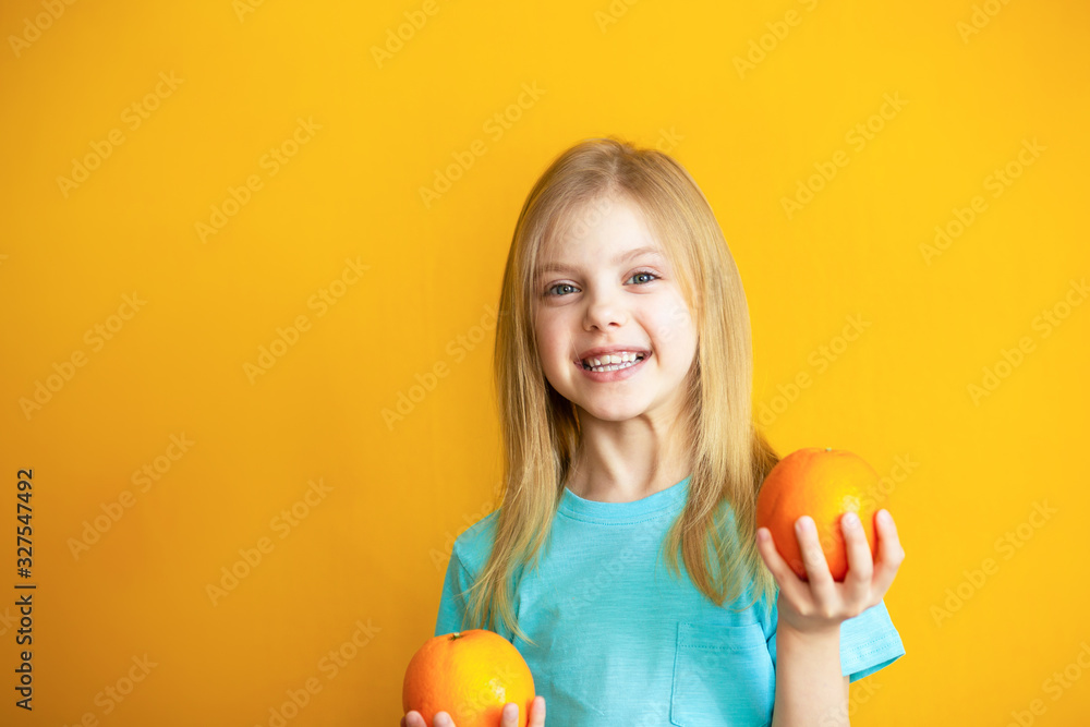 Cute baby 8 years old on an orange background, blonde pretty girl with appelsins in her hands smiles Cute baby 8 years old on an orange background, blonde pretty girl with appelsins in her hands smiles