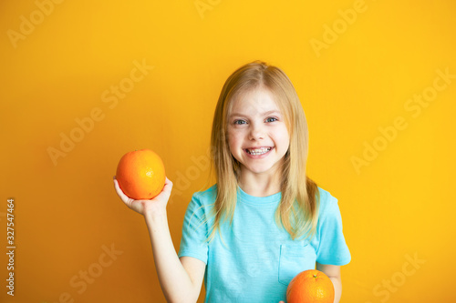 Cute baby 8 years old on an orange background, blonde pretty girl with appelsins in her hands smiles